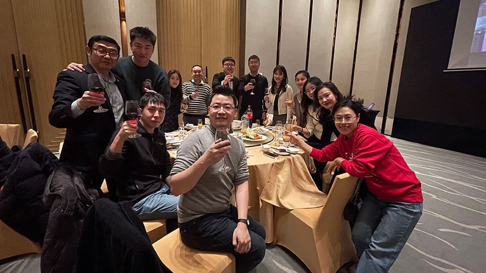 A group of thirteen alumni standing and sitting around a table smiling at one of the University's alumni events in Beijing.